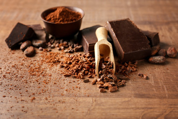 Scoop with aromatic cocoa nibs and pieces of chocolate on wooden background