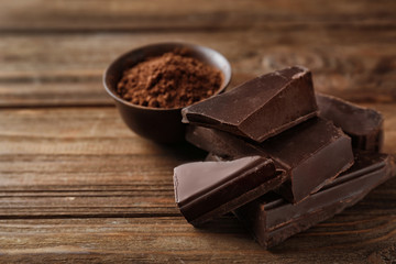 Pieces of tasty dark chocolate and bowl with cocoa powder on background