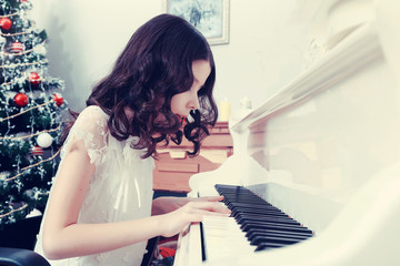 Beautiful girl in a white dress sitting at the piano.