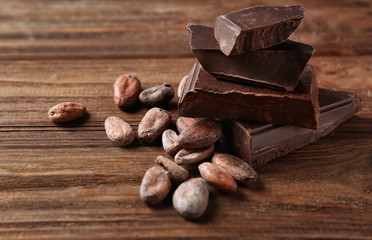 Cocoa beans and pieces of chocolate on wooden background