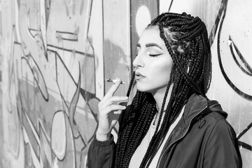 Braided young woman smoking outdoors. With african braids, pierced fashion woman. Converted to black and white, grain added.