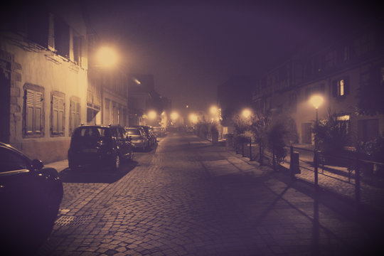 Foggy street of the old city with cars. ancient cobbled street and a blurred light of the street lamps