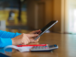 Fototapeta premium Pretty Young womans hands holding and using tablet for online shopping, bill, pencil and calculator on the table. Online payment. Female working on tablet in a cafe.