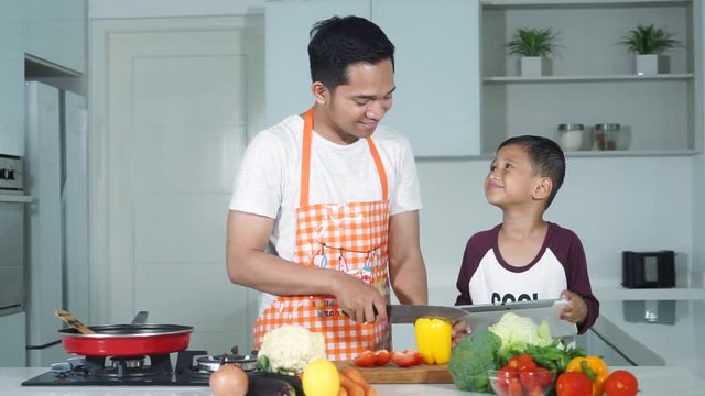 JAKARTA, April 12, 2017: Little boy and his father cooking vegetables in the kitchen at home