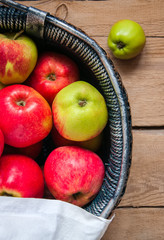 Top view of fresh garden red and green apples in a gray basket on a wooden background. Dark rustic style.