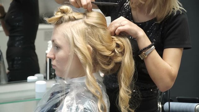 Portrait of a young woman in a beauty salon: creating a magnificent setting from curls. A blonde in a hairdresser does a beautiful hairstyle. Hair care and creating an image.