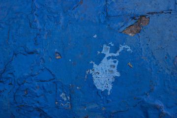  Cracks on an old concrete wall painted in blue. The paint peeling off