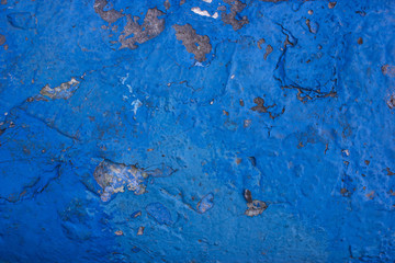  Cracks on an old concrete wall painted in blue. The paint peeling off