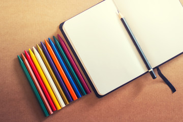 Set of colorful pencils with open blank notebook and carbon pencil for sketching on the light brown...