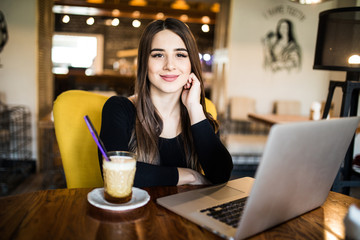 Pretty brunette using her laptop in a coffee shop and look at camera
