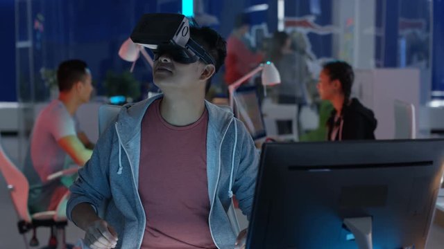  Young computer game designer working at his desk & looking into VR viewer.