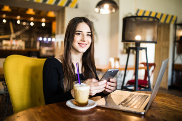 Traveler sending emails with laptop and smartphone during coffee break indoor