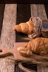 Croissants on board near wheat on wooden sackcloth background. Rustic style.