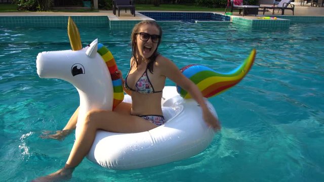 Young Caucasian Woman in Bikini Riding on Big Floating Unicorn in Swimming Pool