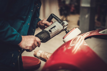 Mechanic polishning car body details in restoration workshop