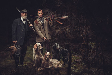 Two hunters with dogs and shotguns in a traditional shooting clothing. © Nejron Photo