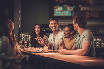 Cheerful multiracial friends eating in pizzeria.