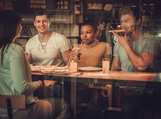 Cheerful multiracial friends eating in pizzeria.