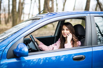 Young woman with hand on steering wheel using mobile phone while driving on road