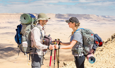 Couple tourists backpackers standing desert mountain peak ridge.