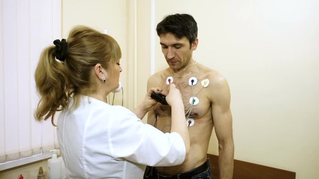 Holter monitor device. Female doctor attaching electrodes on patient's chest to daily monitoring of an electrocardiogram. HD