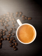 Cup of hot espresso coffee and crop beans on wood background