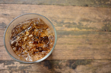 Glass of cola with ice cubes on wood background