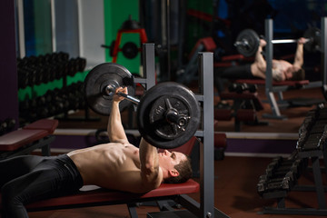 Obraz na płótnie Canvas Brutal athletic man pumping up muscles on bench press