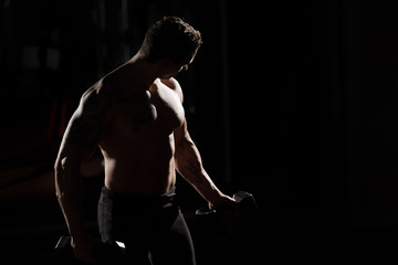 Fototapeta na wymiar Handsome power athletic guy bodybuilder doing exercises with dumbbell. Fitness muscular body on dark background.