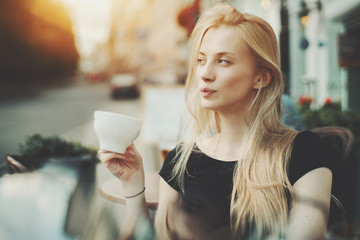 Beautiful adult blonde lady is tasting delicious tea while sitting in street bar on springtime day,...