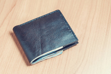 Black wallet with money on wooden table.
