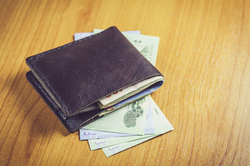 Black wallet with money on wooden table.