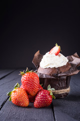Cupcake decorated with strawberries and cream on a dark wooden background
