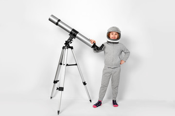 Happy child girl dressed in an astronaut costume standing beside the telescope