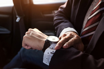 Handsome businessman looking on wrist watch in car