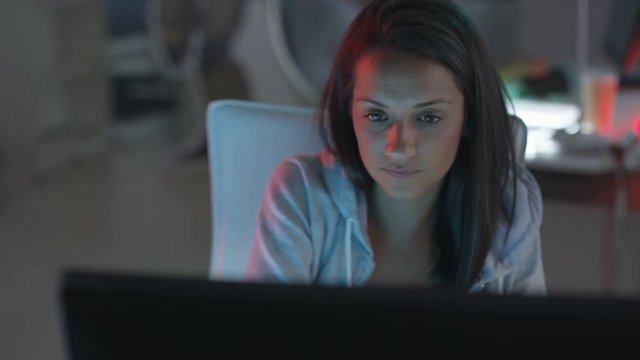 Young technology startup company, woman watching computer screens with colleagues working in background. 