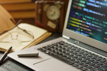 Laptop with programming code , book , pen and  clock at office desk. Low depth of field.