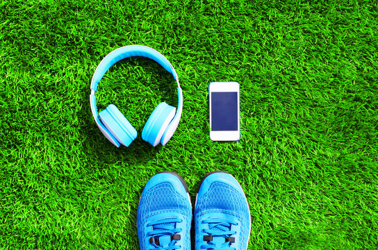 Blue a headphones and white smartphone with sports sneakers shoes on a green grass textured background, top view, flat lay photo