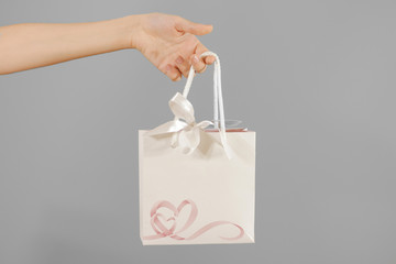 Blank white paper gift bag with hearts mock up holding in hand. Empty plastic package mockup hold...