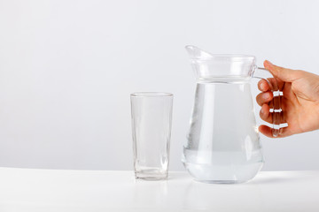 Hand pouring water from glass jug to glass against white background