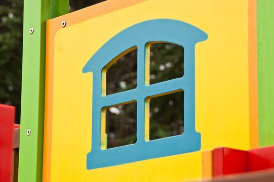 Blue square window with arch, fragment of yellow children wooden house - slide at the playground outdoors.   