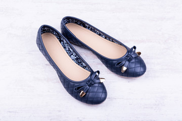 Pair of dark blue ladies' flat shoes on white wooden background.
