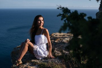 Beautiful thinking woman on the stone on blue sea and sky background in sunset.