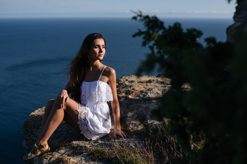 Beautiful thinking woman on the stone on blue sea and sky background in sunset.