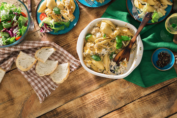 Dinner table with pasta, salad and wine on wooden table