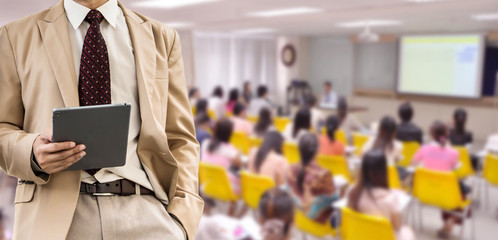 businessman using the tablet, blurred of conference hall or seminar room with attendee background.