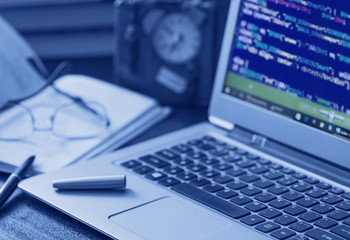 Laptop with programming code at office desk. Tinted image. Low depth of field.