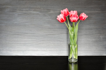 Five pink tulips in a transparent vase on a black table, space for text