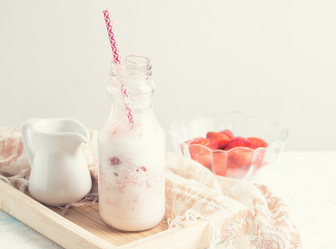 Strawberry milkshake in glass bottle with ingredients on white table