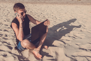 Young man with laptop computer and mobile phone on the beach. Downshifting and freelance concept.